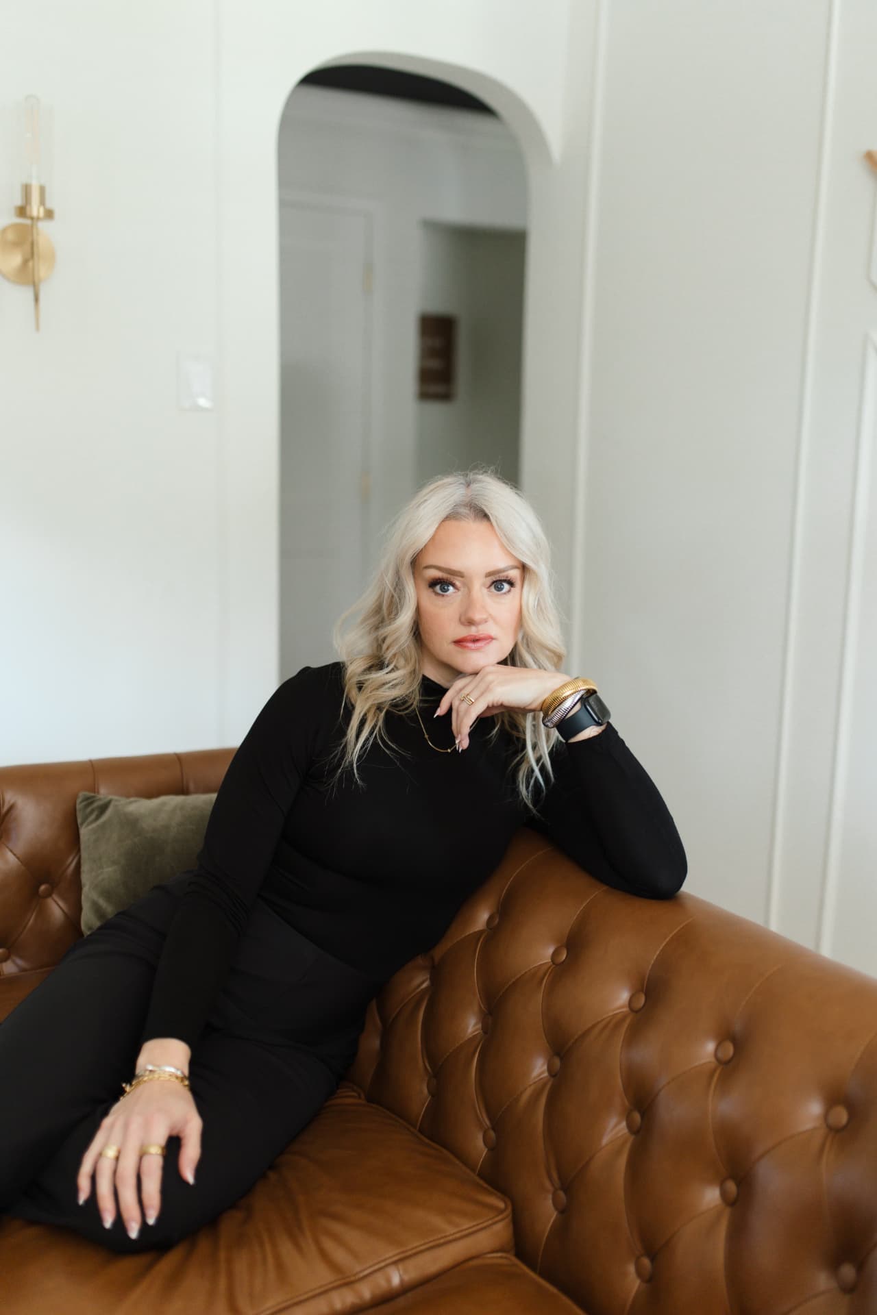 April Martini seated on a leather sofa, hand at her chin, looking directly at the camera